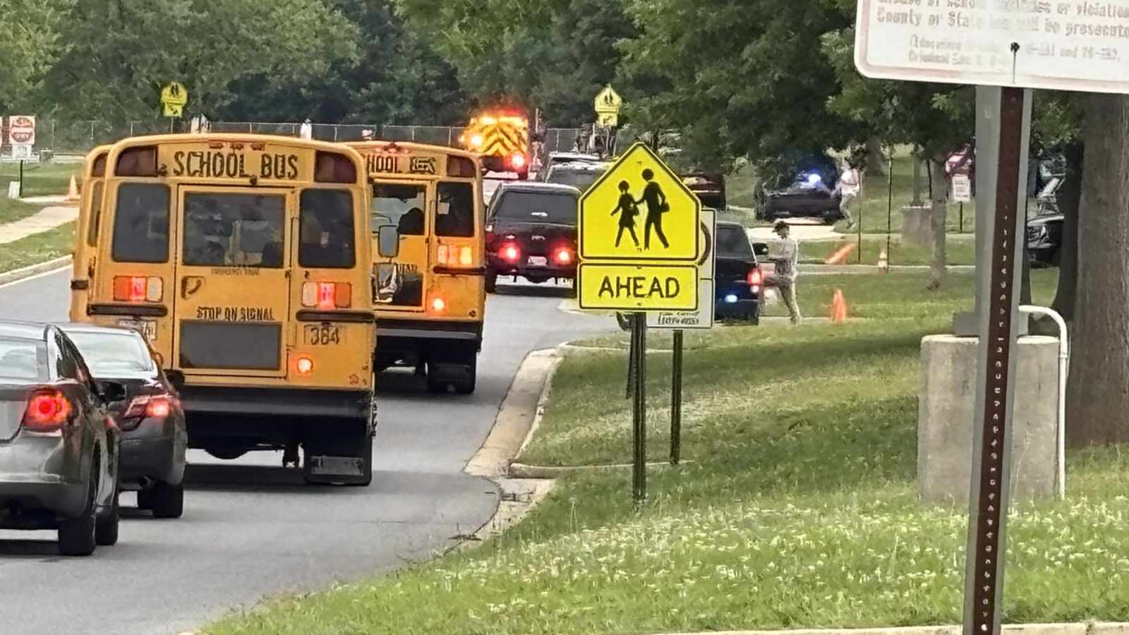 Yellow school buses and emergency vehicles lined up on a road near school grounds