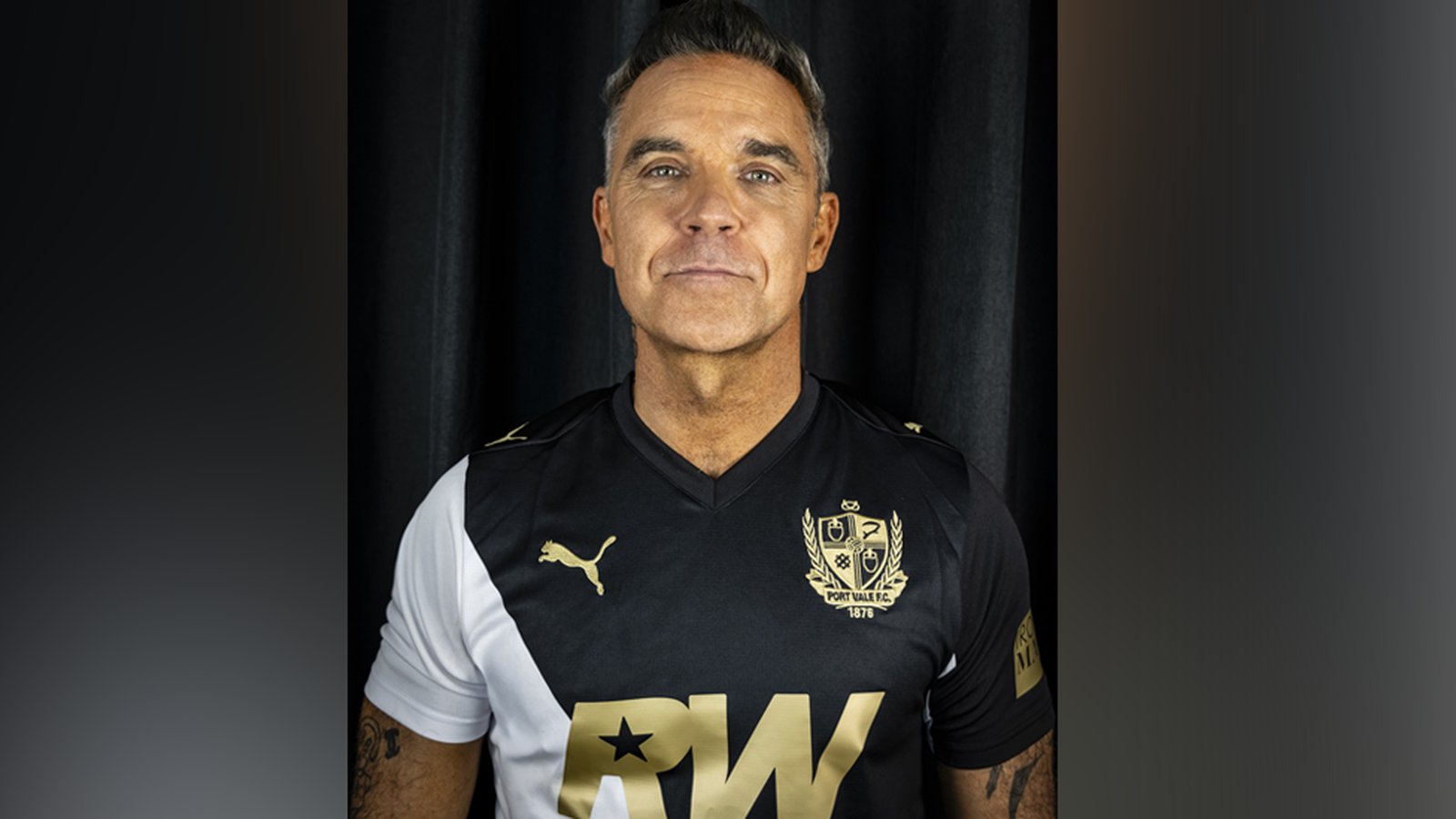Robbie Williams wearing a black and white Port Vale FC football shirt