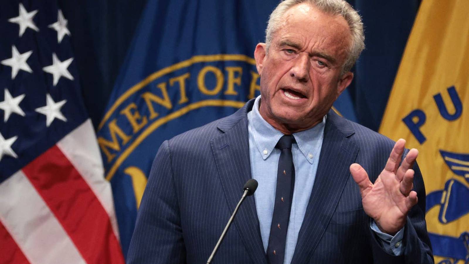 Robert F Kennedy Jr speaking at a podium with American flag background
