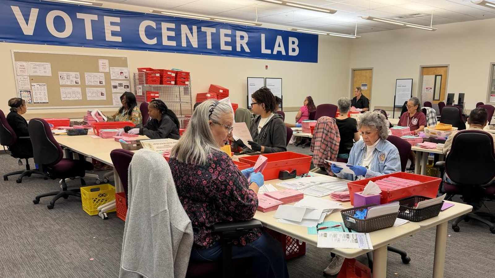 Election workers processing ballots at tables inside a Sacramento County vote center lab