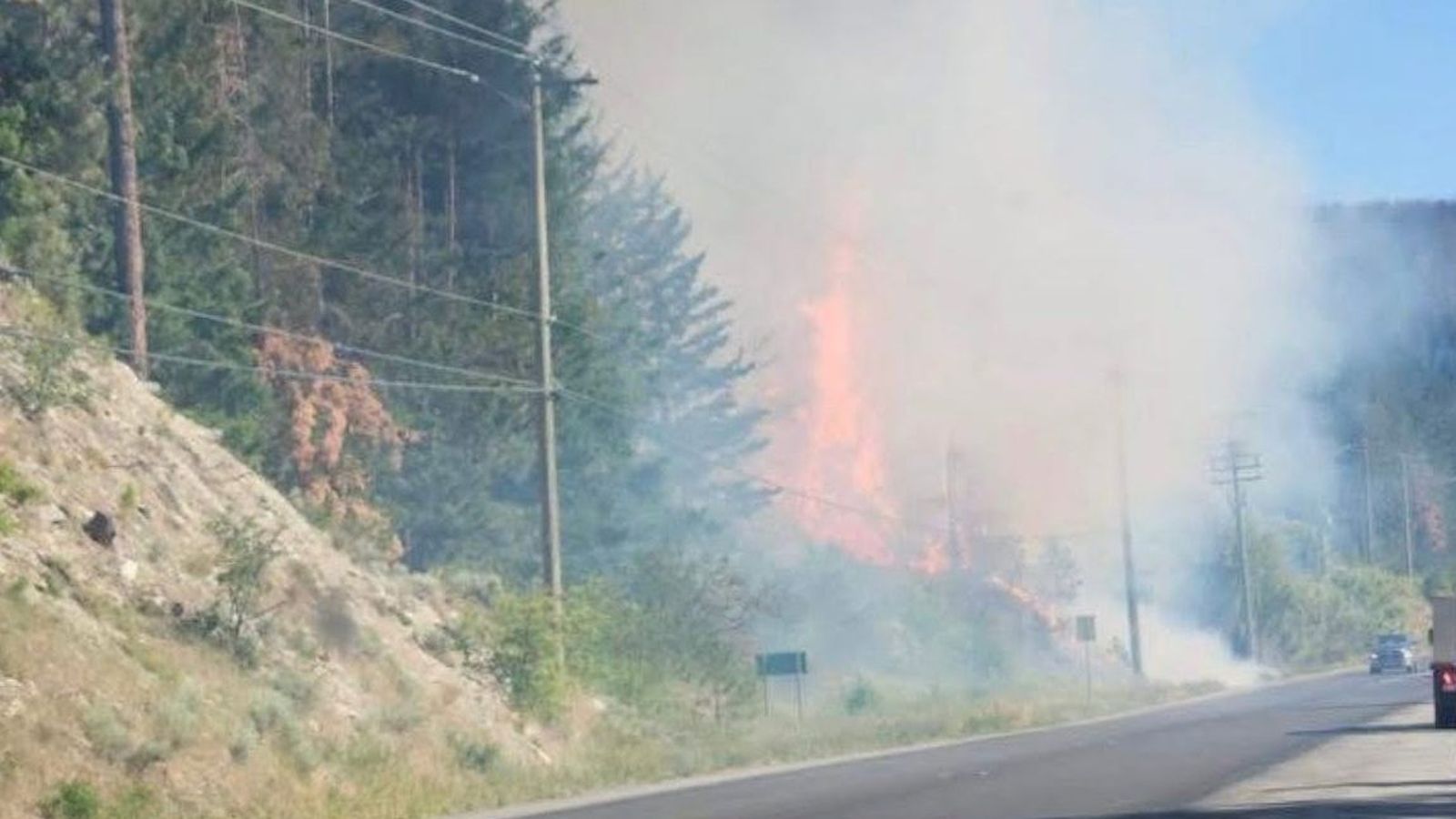 Flames and thick smoke rising from a forest fire beside a highway road