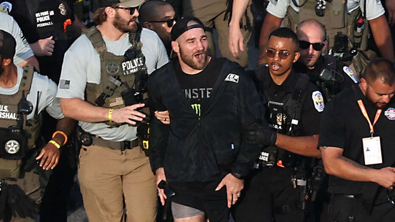 UFC fighter Sean Strickland being escorted by police officers at the Freedom 250 event