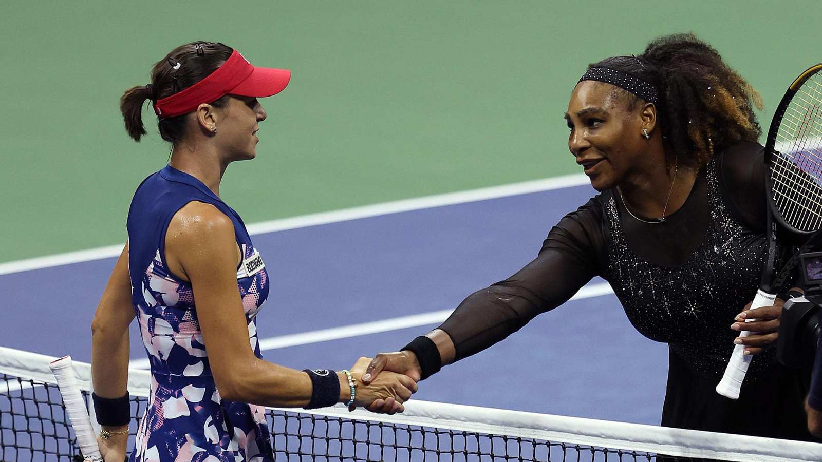 Serena Williams in a black tennis outfit shaking hands with an opponent on court