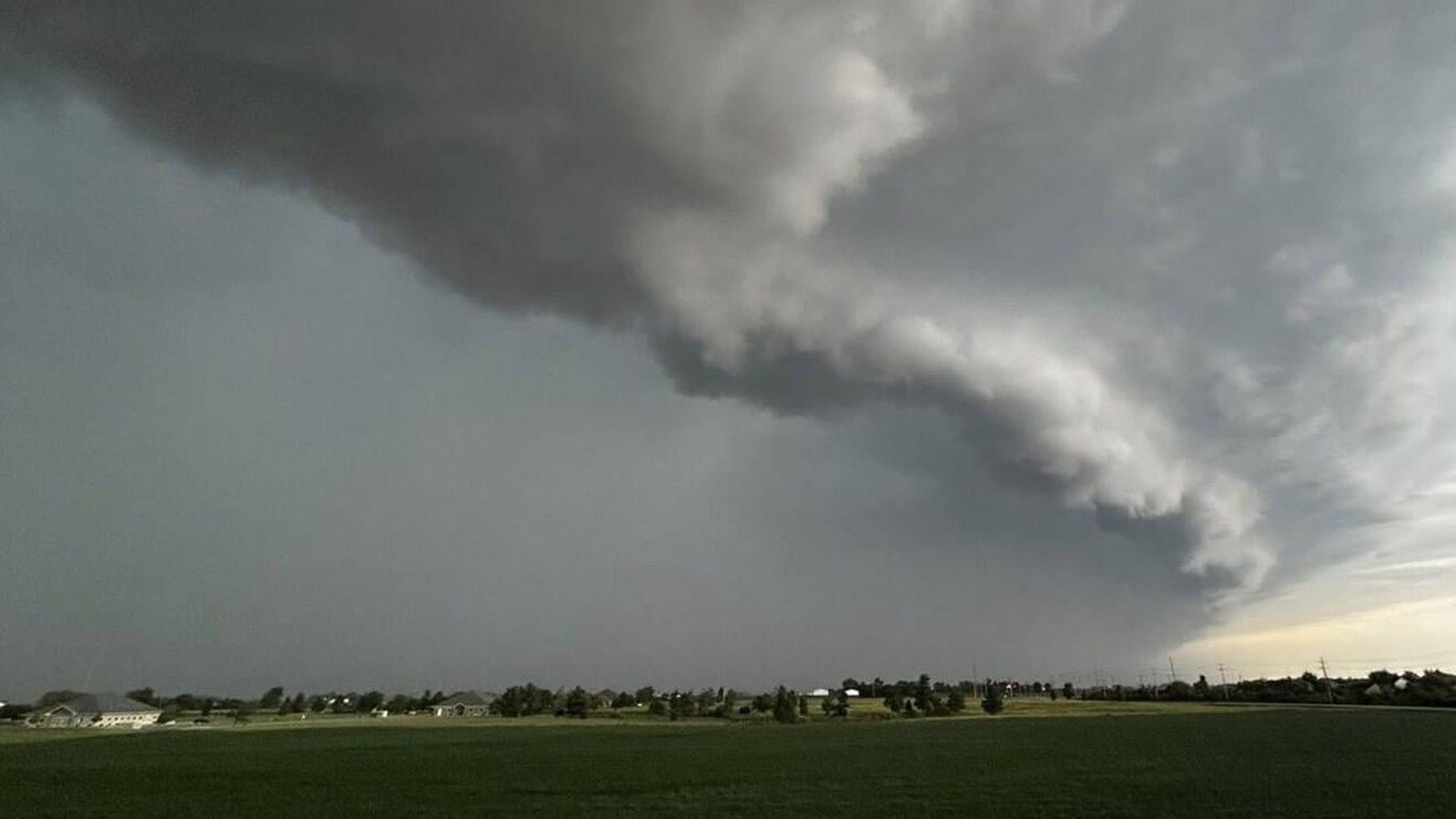 A dark and ominous shelf cloud hangs over a green rural landscape