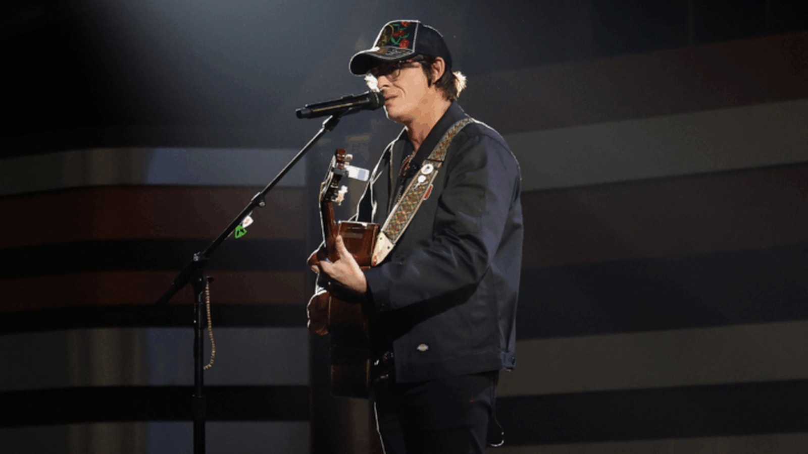 Country singer Stephen Wilson Jr. wearing a cap while playing acoustic guitar on stage