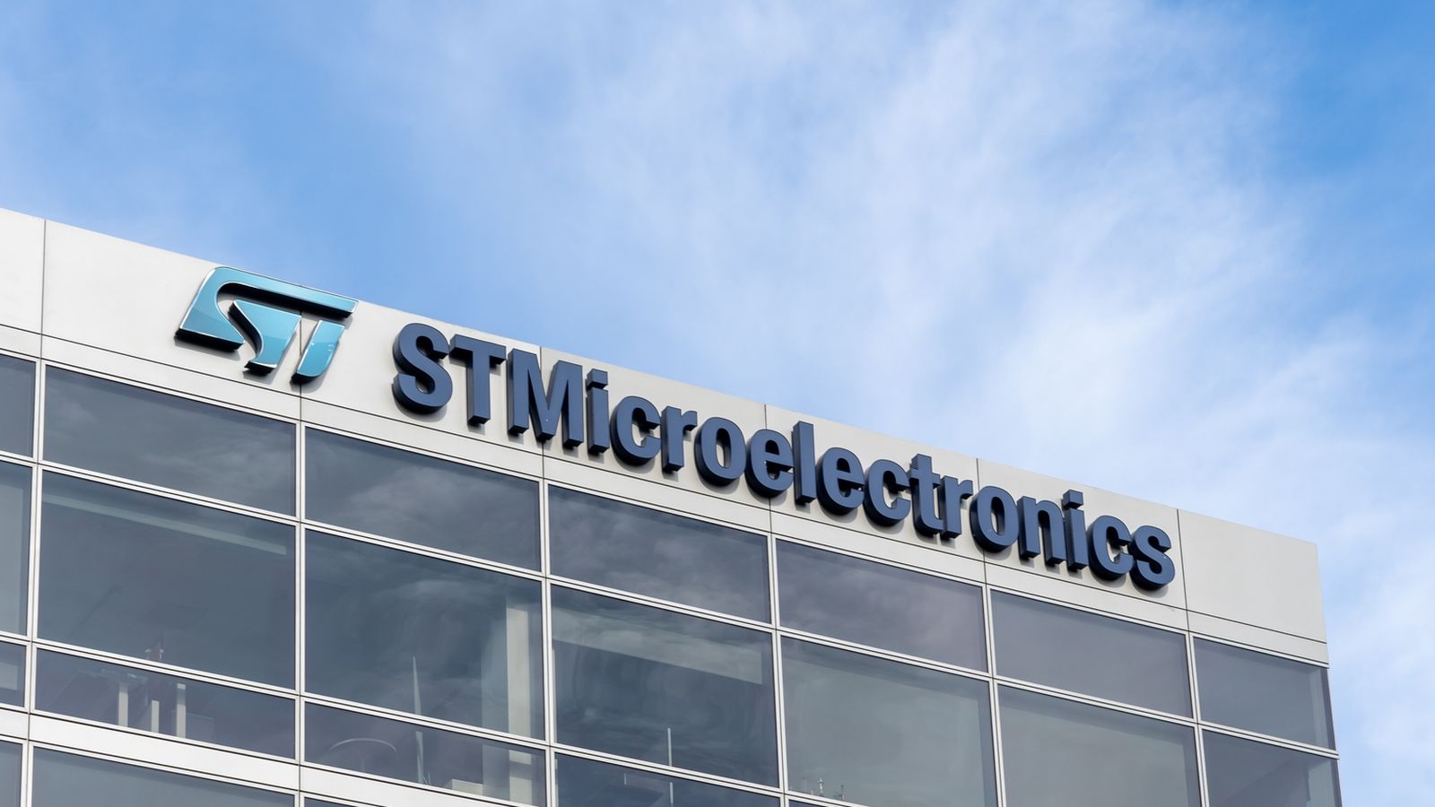 The STMicroelectronics company logo mounted on the exterior of a modern glass office building