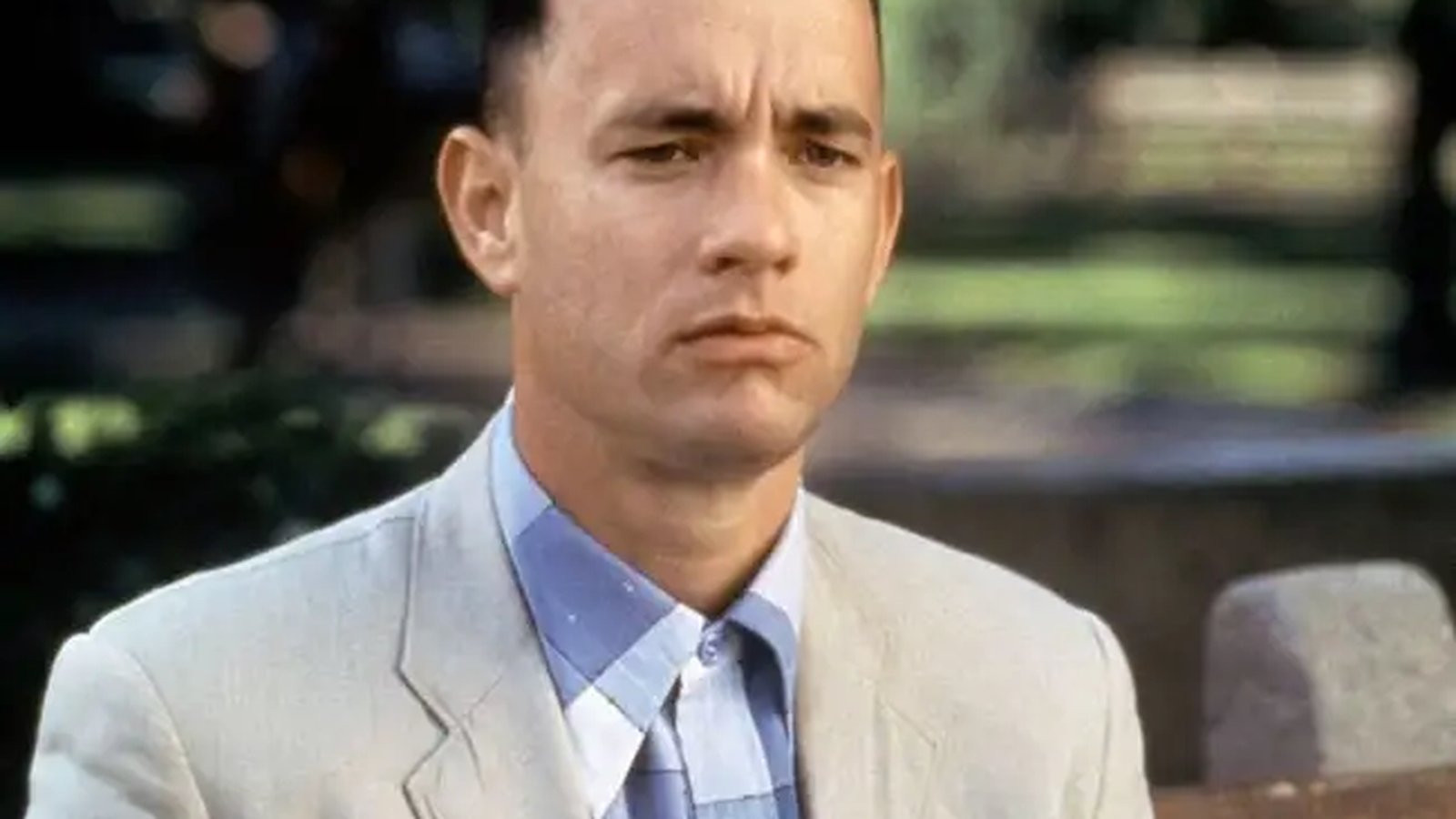 Tom Hanks portraying the character Forrest Gump in a light colored suit jacket