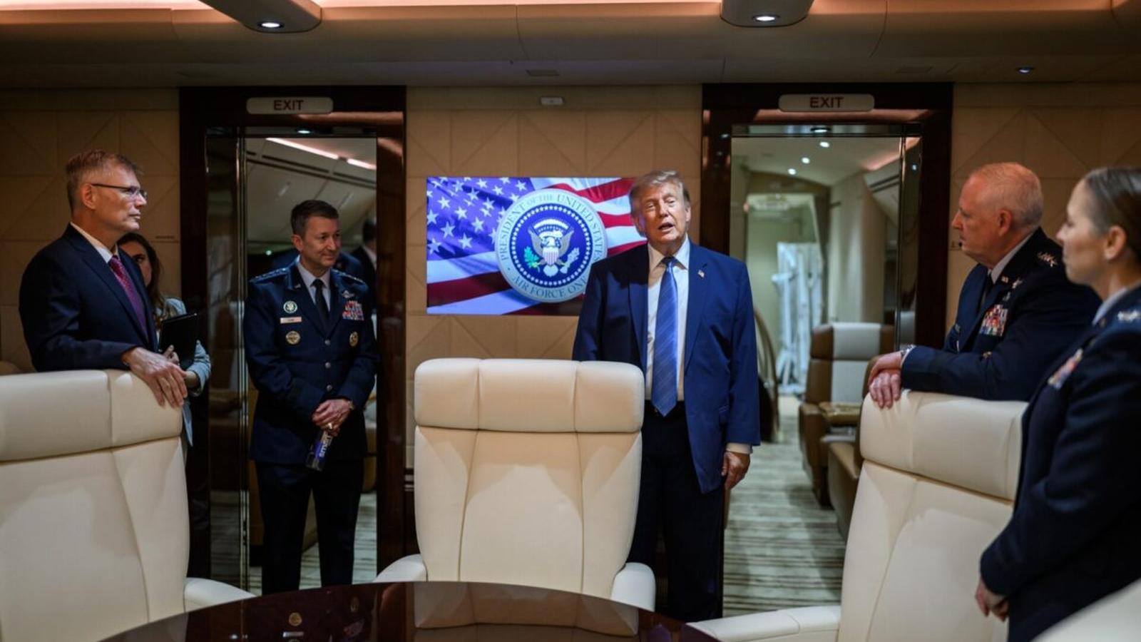 Donald Trump standing in a luxury aircraft cabin with military officials and presidential seal