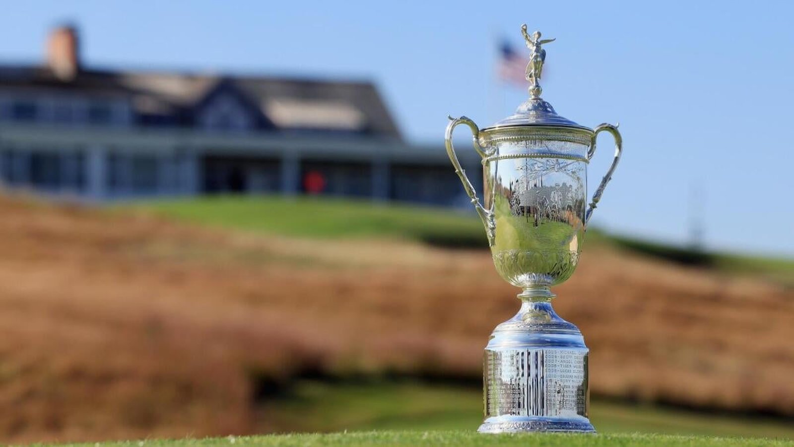 The silver U.S. Open golf championship trophy standing on a green golf course