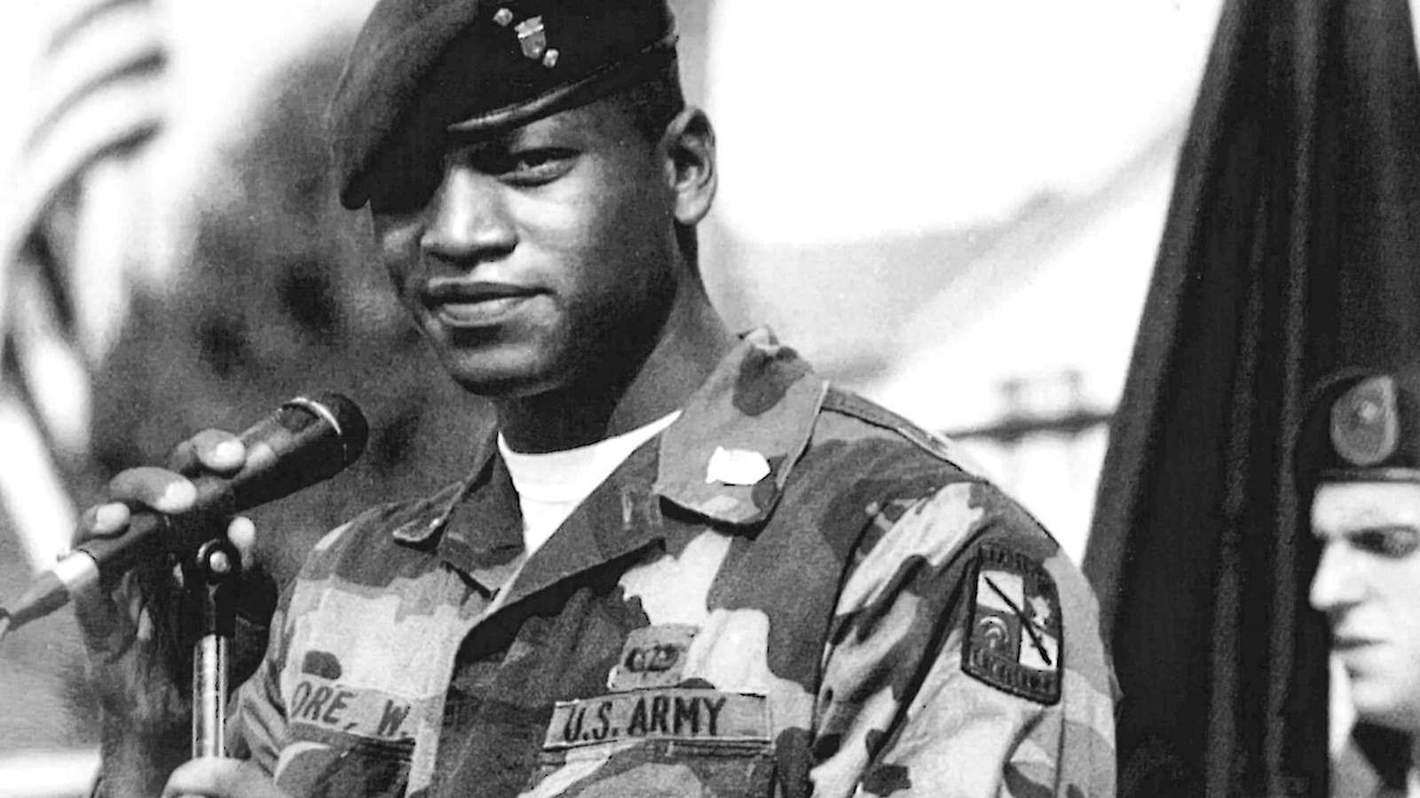 Young Wes Moore wearing a U.S. Army camouflage uniform and beret speaking into microphone