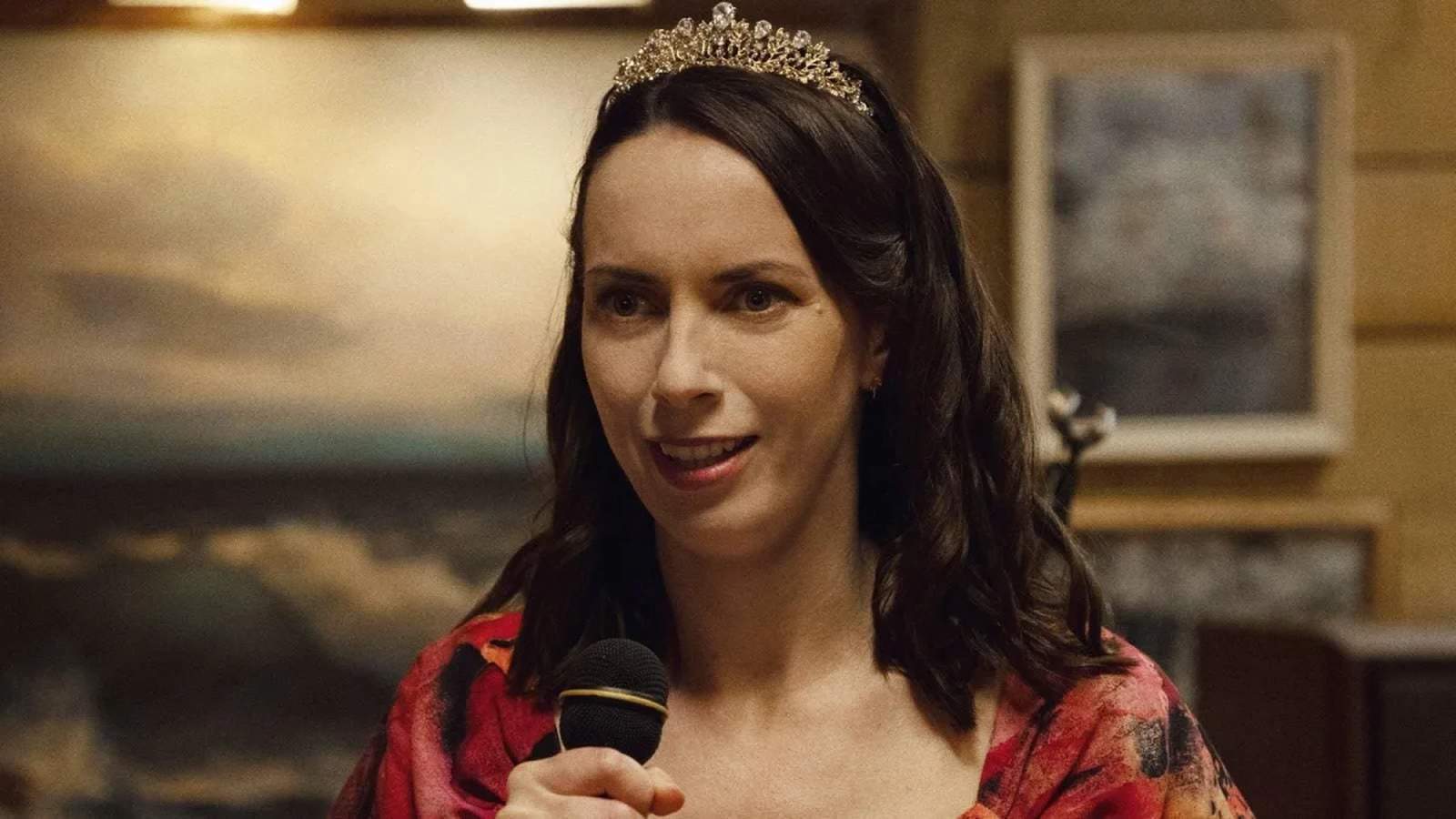 A woman wearing a tiara speaks into a microphone in a scene from Widows Bay