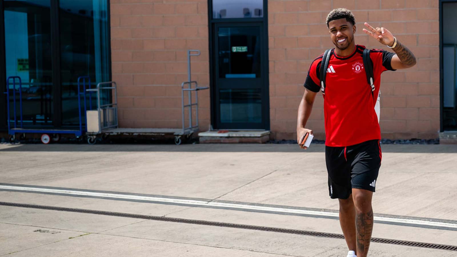 A Manchester United player Andrey Santos in training kit walking and smiling at the camera