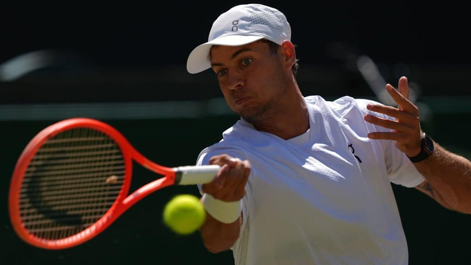 Alex de Minaur wearing a white cap and shirt hitting a tennis ball