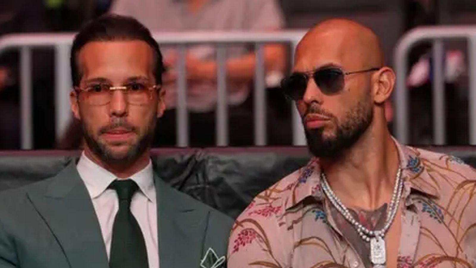 Tristan and Andrew Tate sitting together wearing sunglasses at a public event