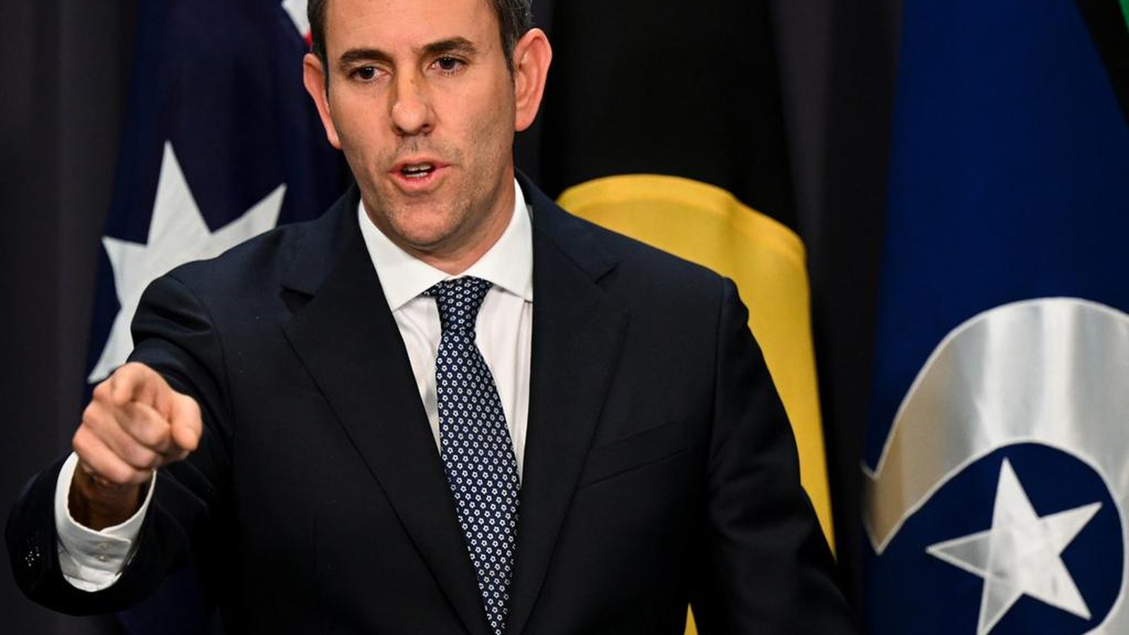 Australian Treasurer Jim Chalmers speaking at a press conference with flags behind him