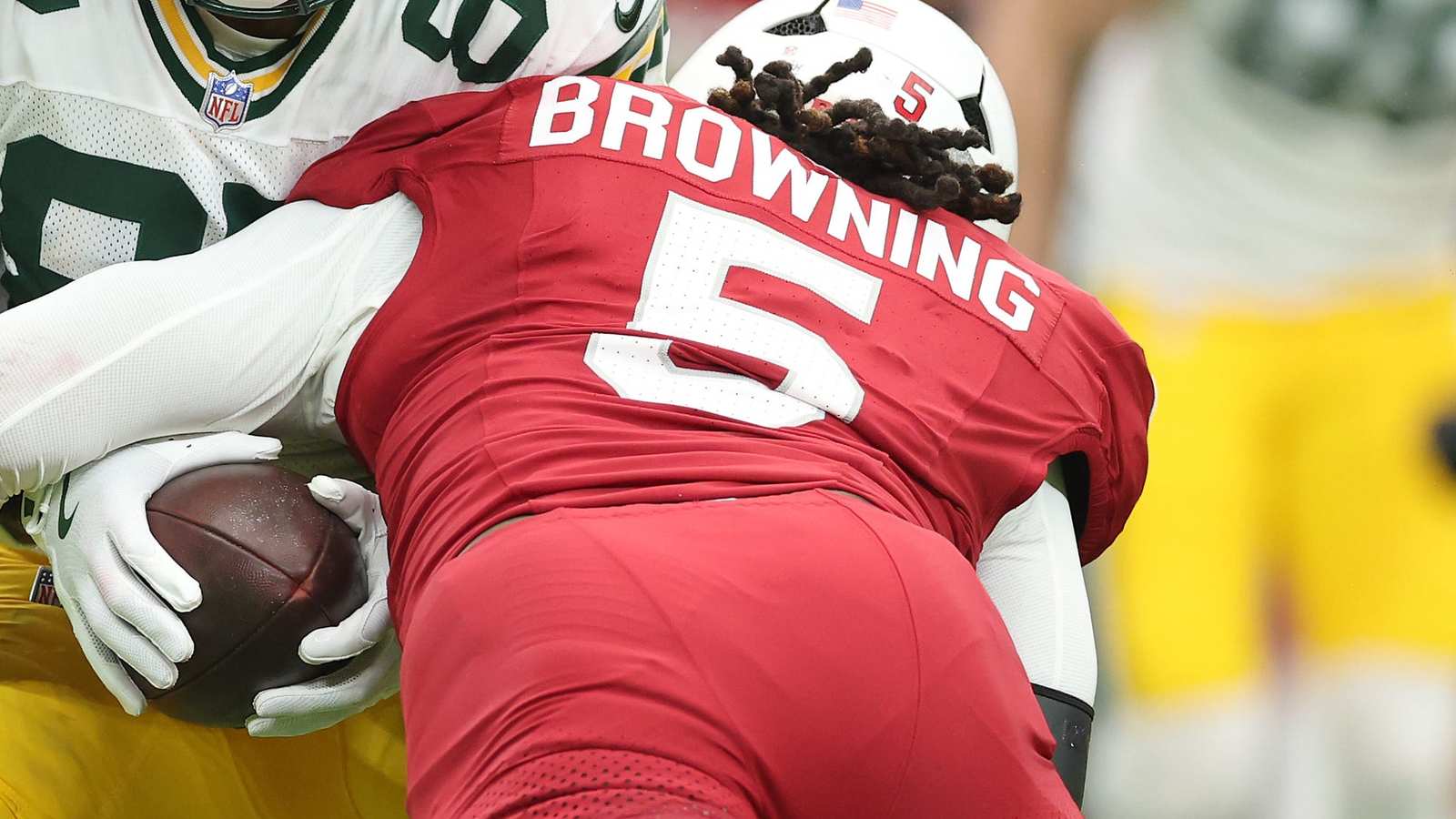 Football player Baron Browning in a red jersey with the number 5 makes a tackle on a player in a gre