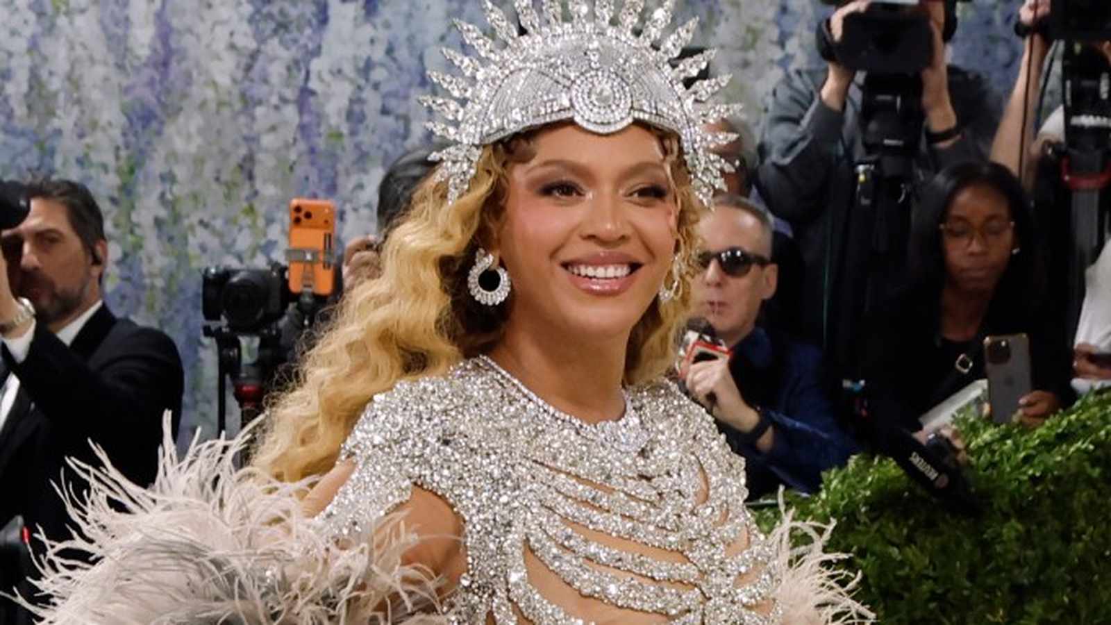 Beyoncé smiling while wearing a silver jeweled headpiece and matching dress at event
