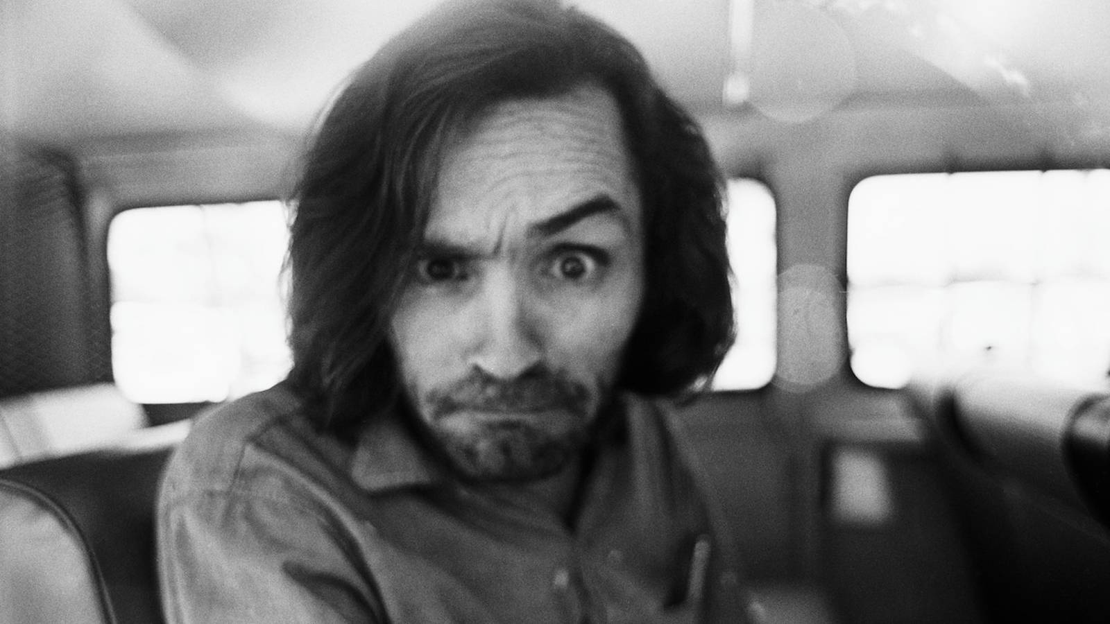 A black and white close up portrait of Charles Manson looking intensely forward