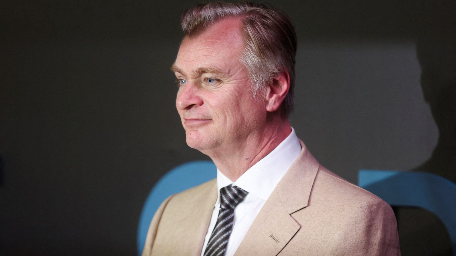 Director Christopher Nolan wearing a tan suit and tie looking to the side