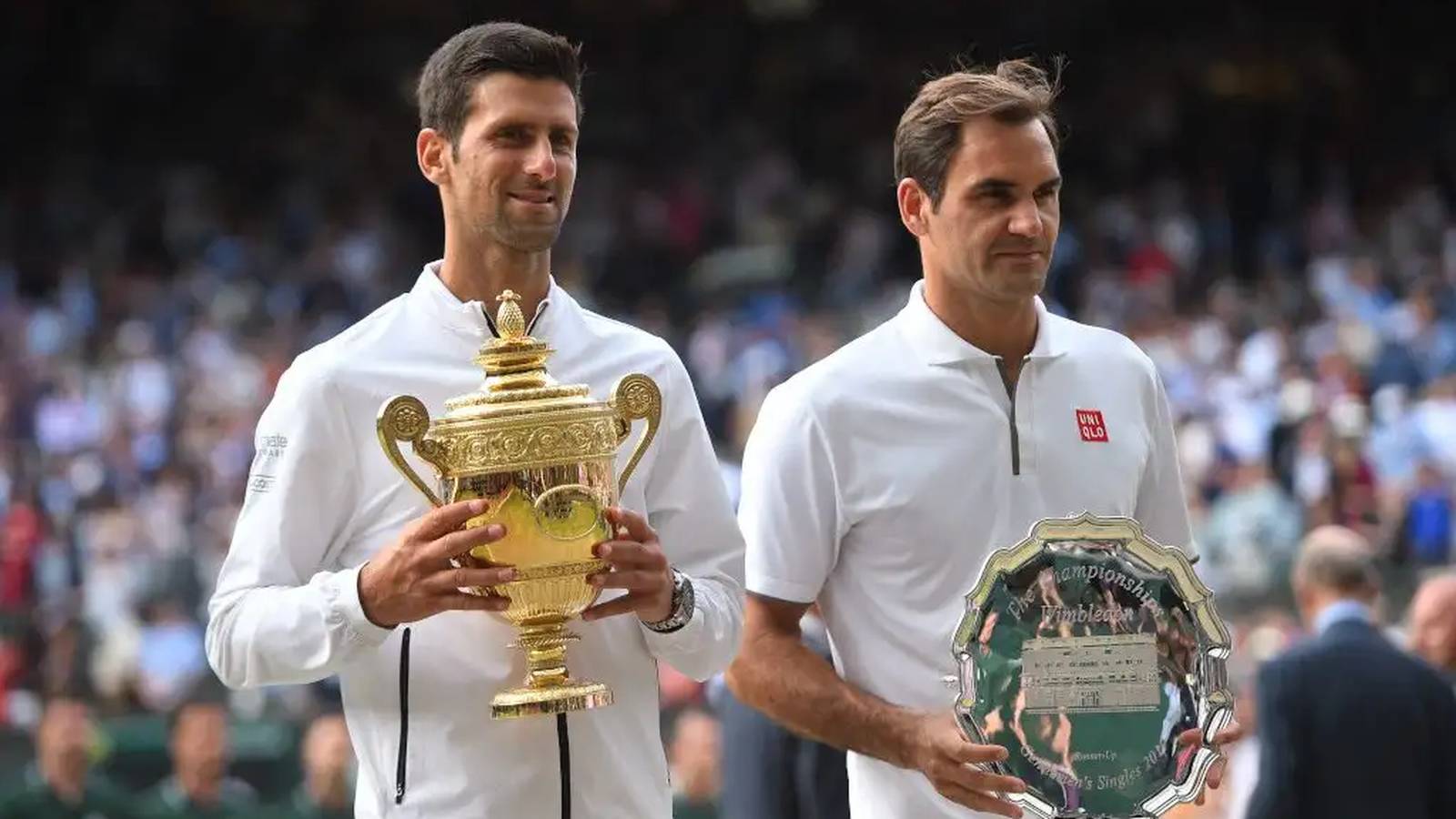 Novak Djokovic holding the Wimbledon trophy next to runner-up Roger Federer on court