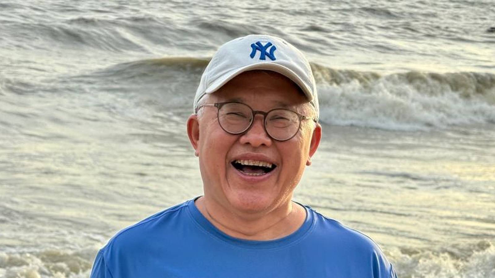Ezra Jin wearing a New York Yankees baseball cap smiling on a beach