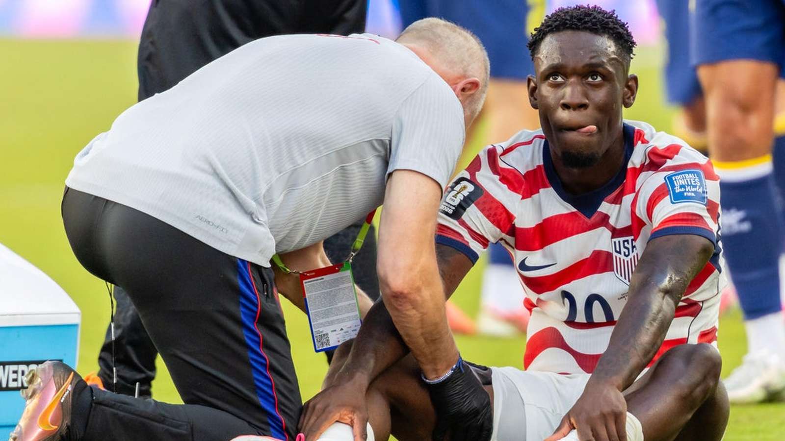 Folarin Balogun sitting on the pitch in a USMNT jersey receiving medical treatment