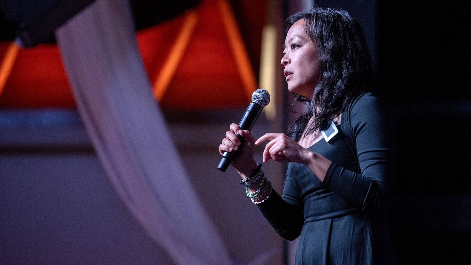 Francesca Hong speaking into a microphone while wearing a dark dress on stage