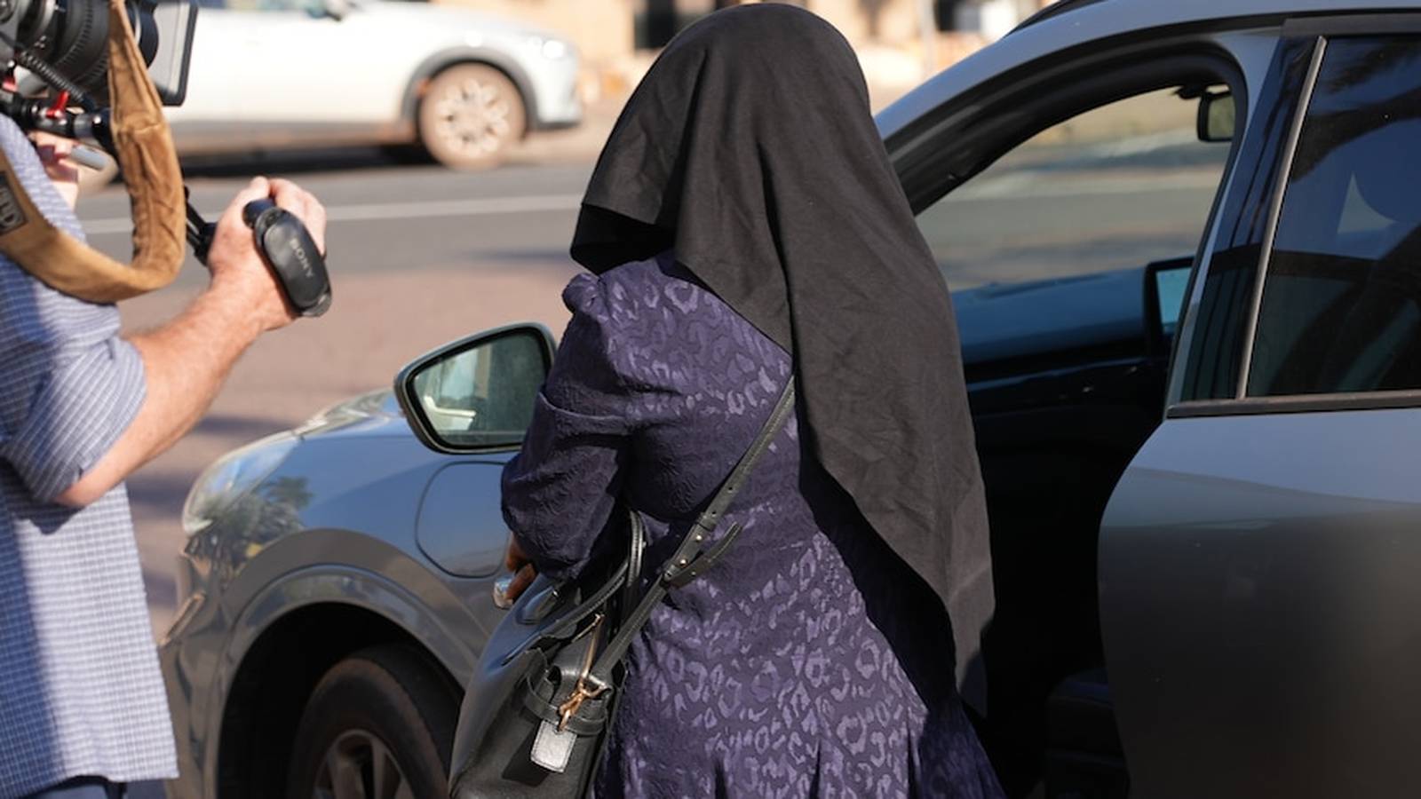 A woman wearing a black head covering and patterned dress entering a car
