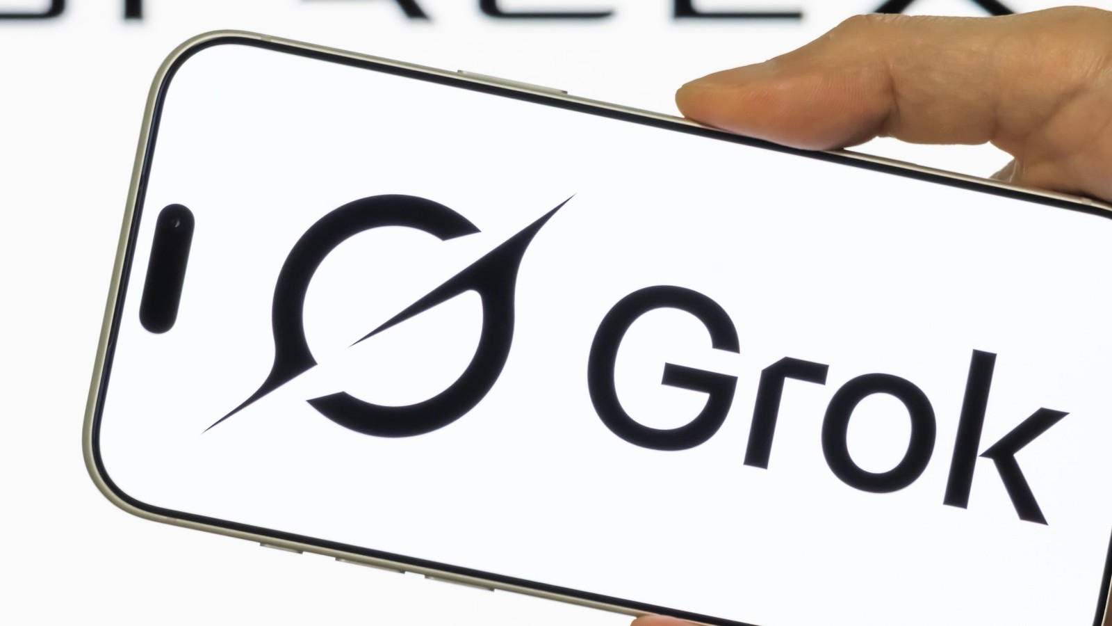 A hand holding a smartphone displaying the Grok AI logo with SpaceX branding visible