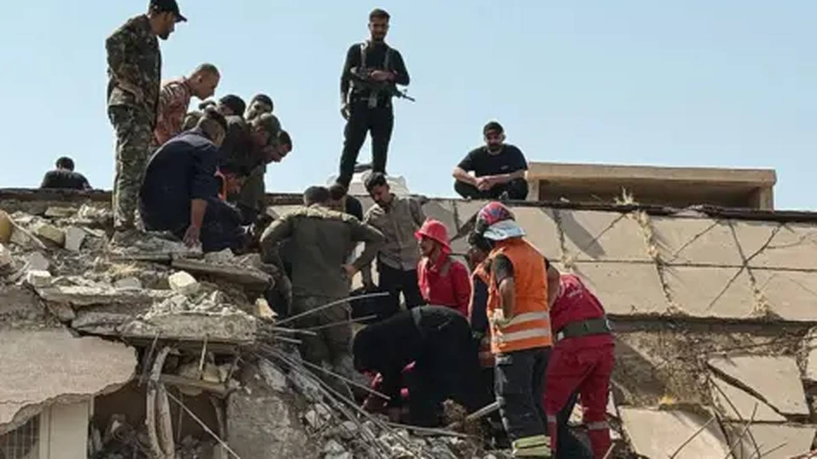 Rescue workers and armed personnel searching through rubble at a damaged building in Iraq