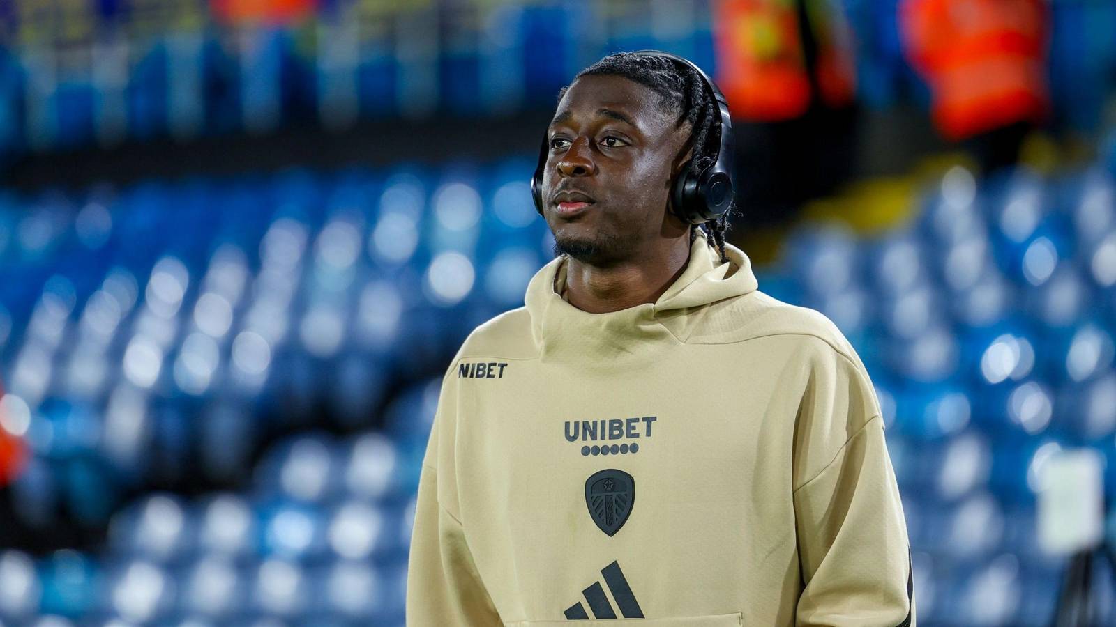 James Debayo wearing a beige Leeds United training hoodie with headphones at a stadium
