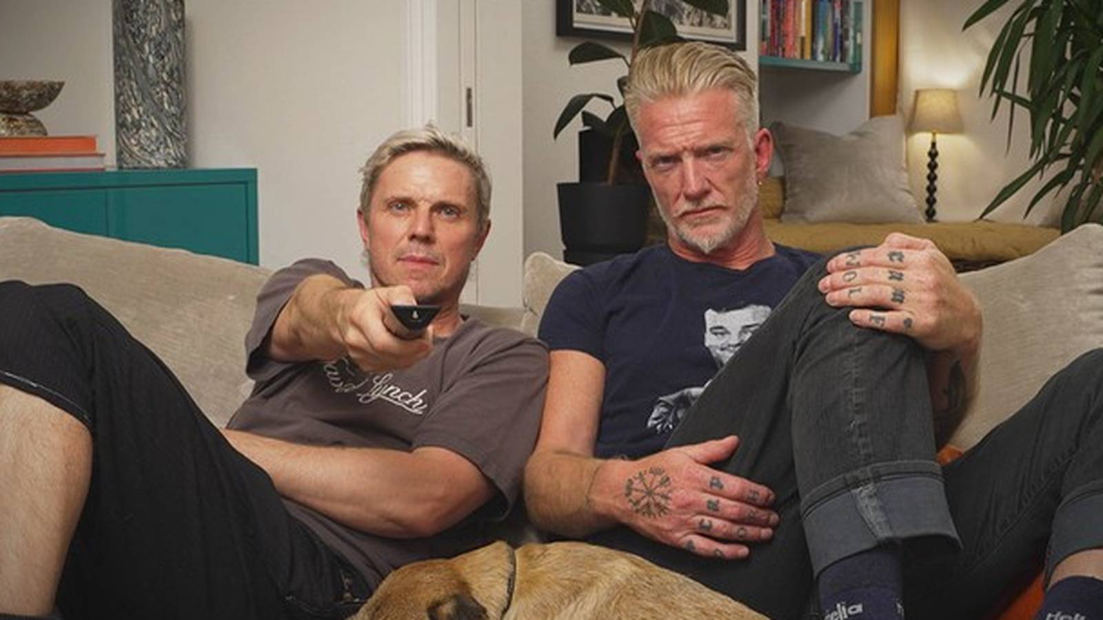 Josh Homme and Jake Shears sitting on a sofa watching television together