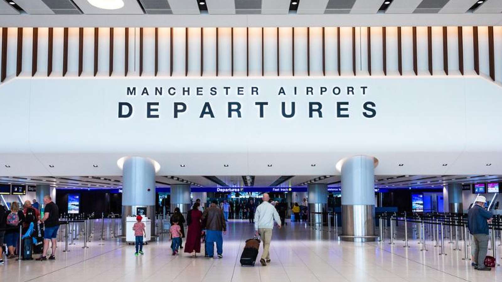 Travelers walking through the modern Manchester Airport departures hall with signage visible above