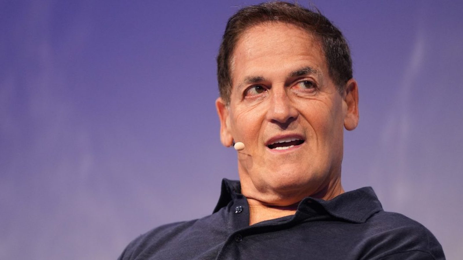 Mark Cuban wearing a dark polo shirt speaking at a public event