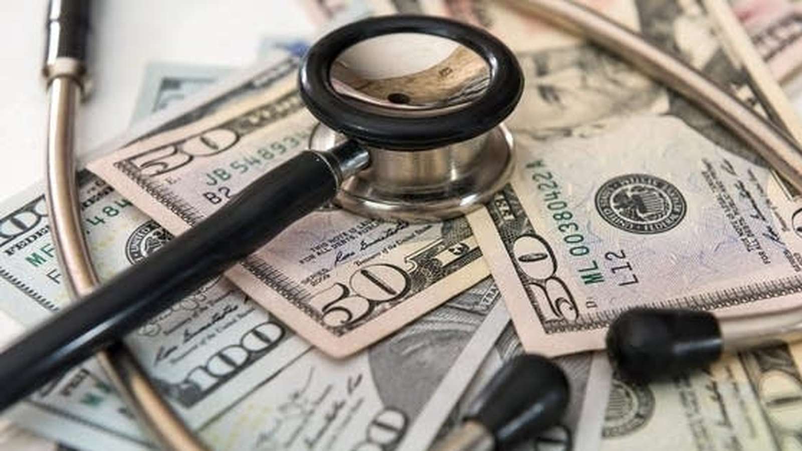 A medical stethoscope resting on a pile of various United States dollar bills
