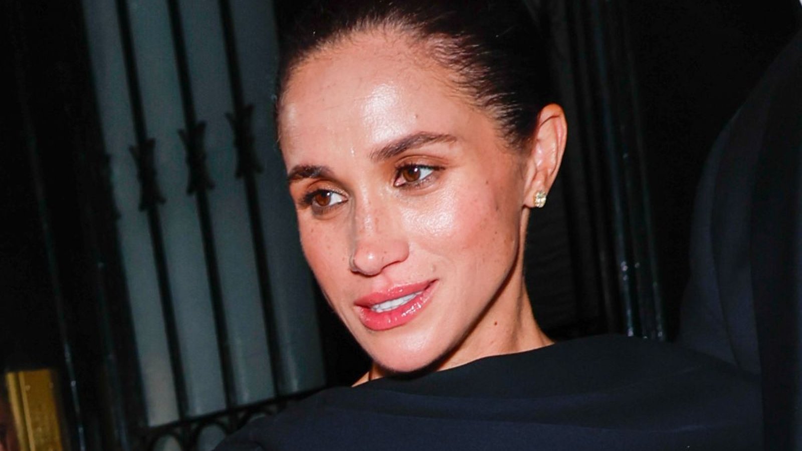 Meghan Markle looking forward with a neutral expression in a dark setting