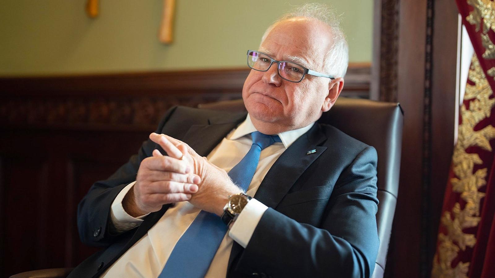 Minnesota Governor Tim Walz sitting in a chair wearing a suit and tie