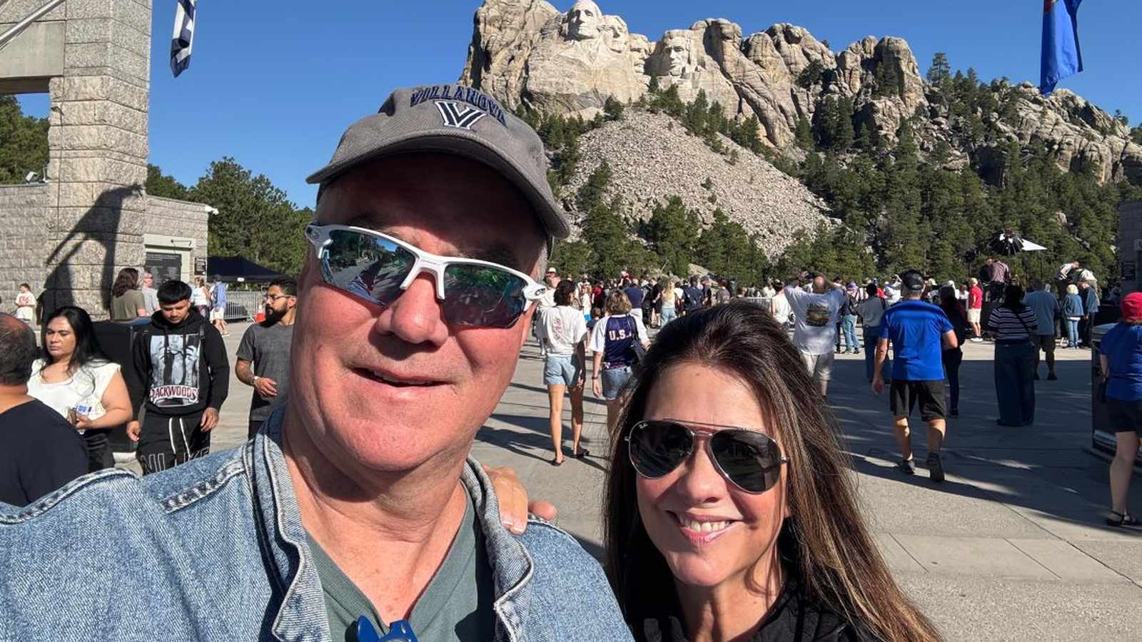 A couple taking a selfie in front of the crowded Mount Rushmore National Memorial