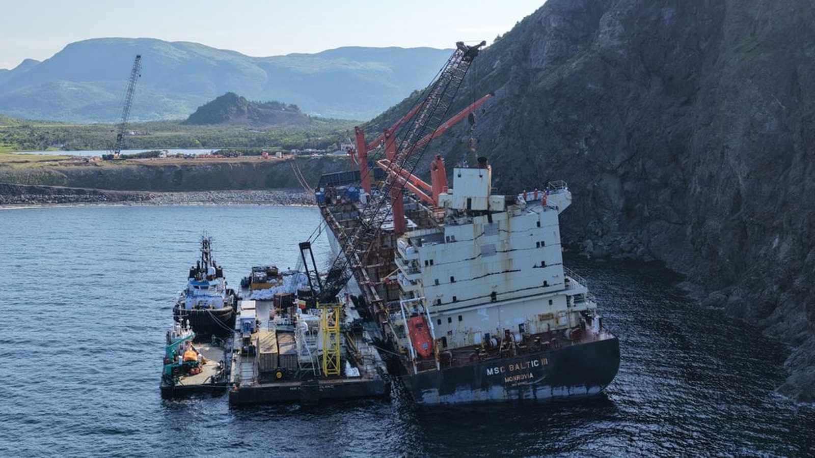Aerial view of salvage cranes dismantling the MSC Baltic III wreck near cliffs