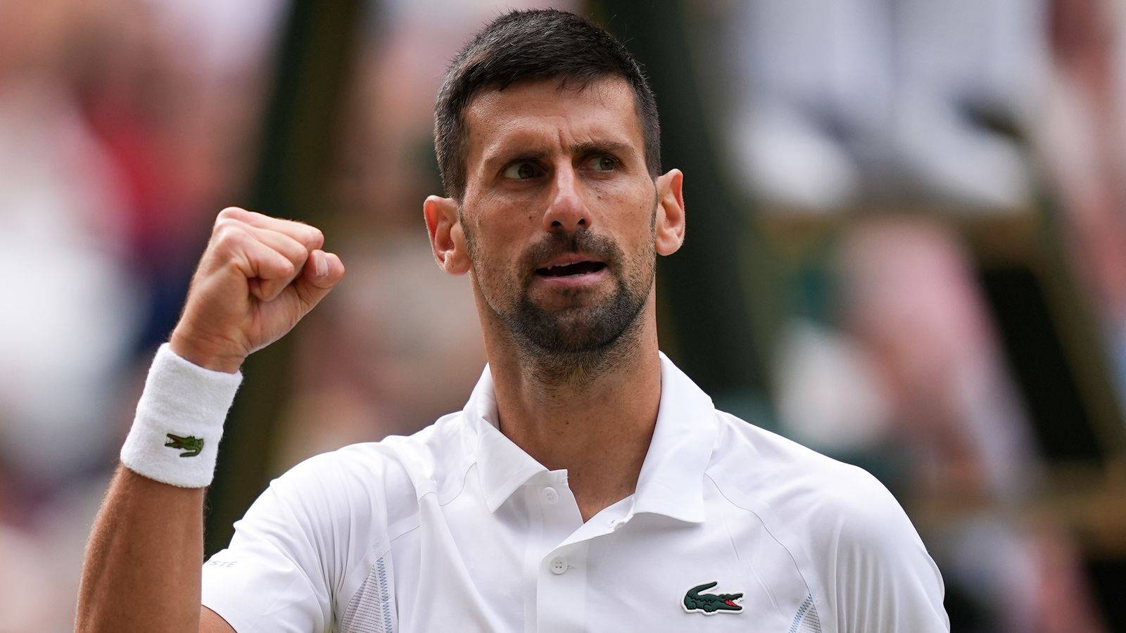 Novak Djokovic clenches his fist in celebration while wearing a white tennis shirt