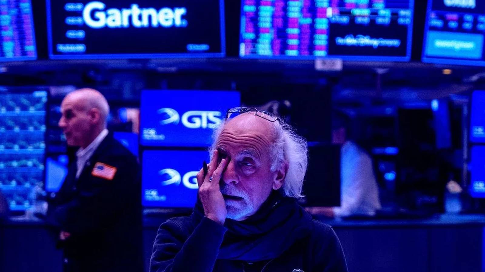 A trader with glasses rubs his eye while working on the New York Stock Exchange floor
