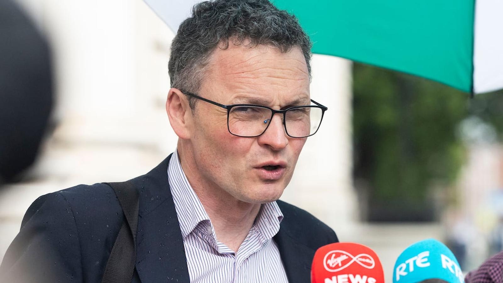 Irish Minister Patrick ODonovan wearing glasses and a suit speaking to news reporters