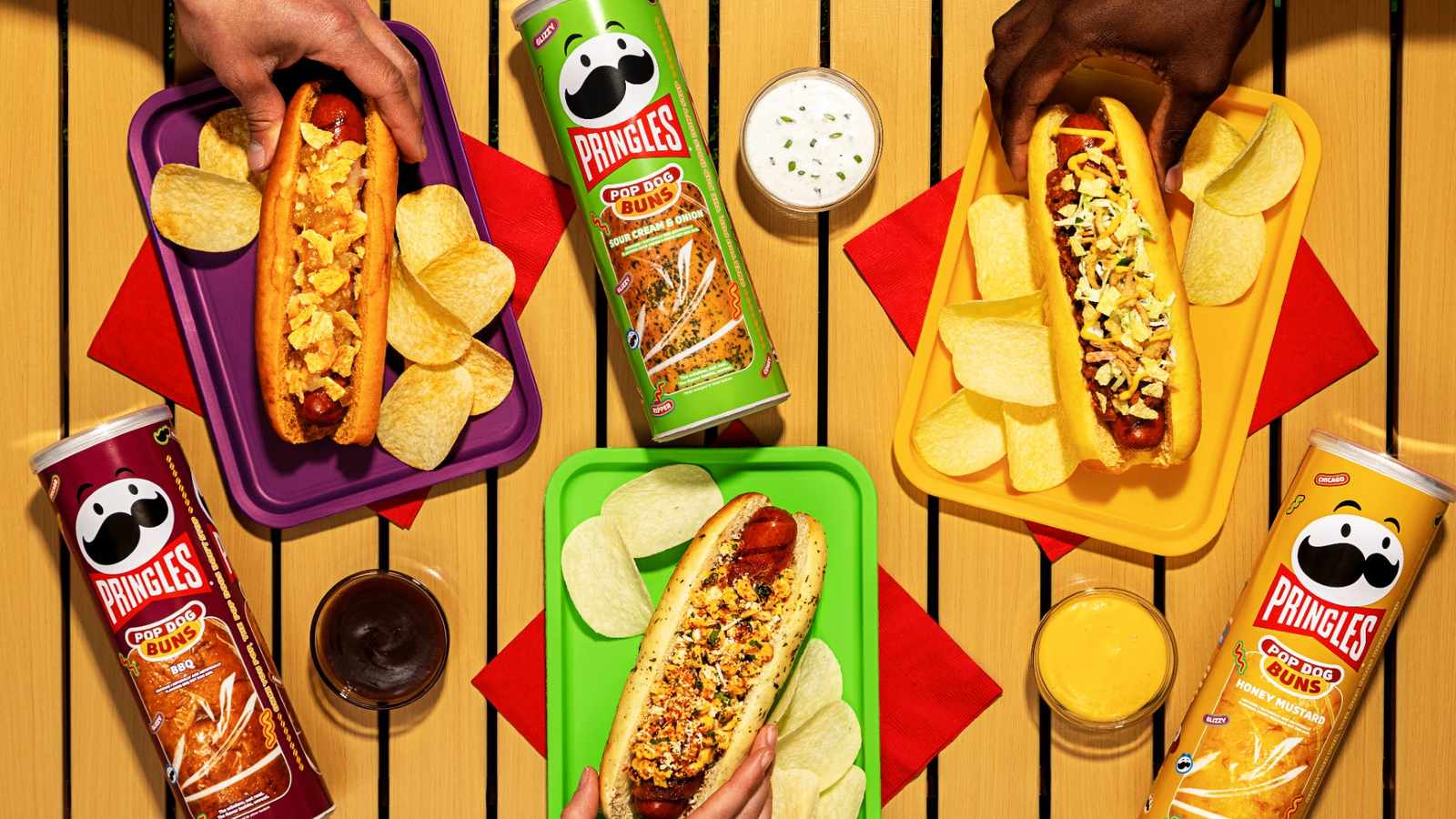 Three hot dogs in Pringles flavored buns surrounded by Pringles chip canisters on table