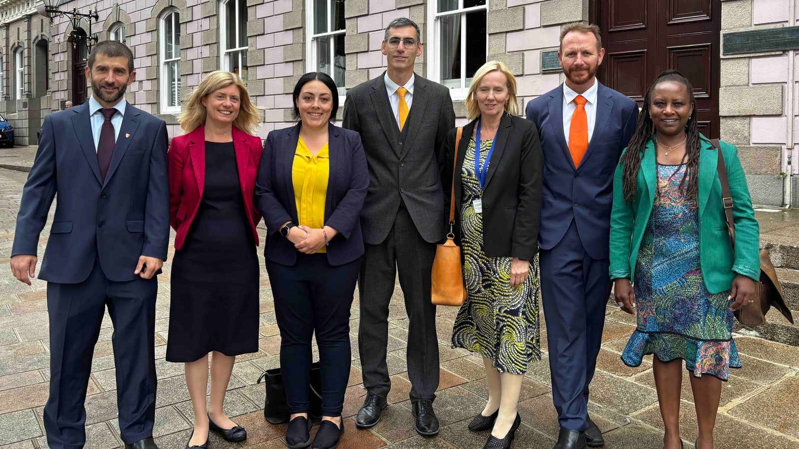 A group of six Reform Jersey politicians standing together outside a stone building