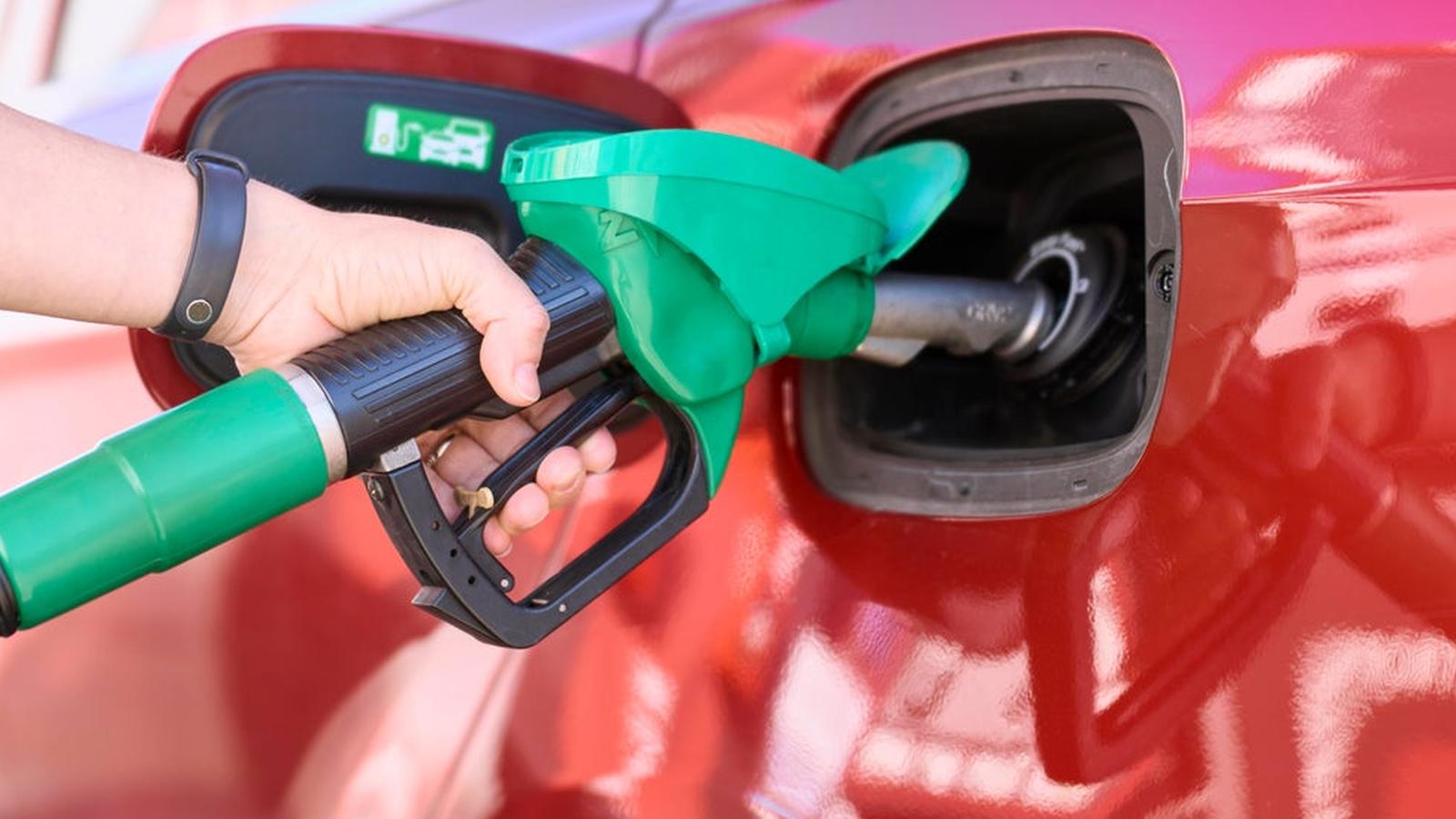 A hand holding a green gas pump nozzle filling a red car tank