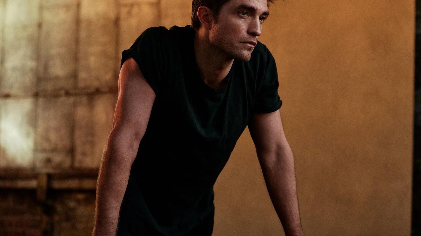 Robert Pattinson posing in a black t-shirt against a warm textured background