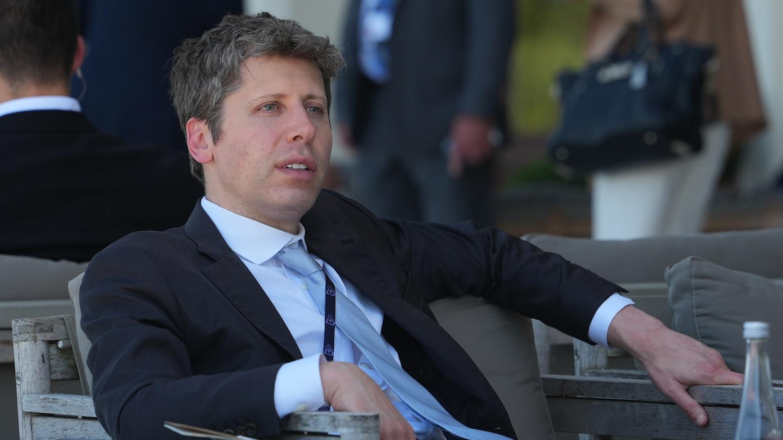Sam Altman wearing a suit and tie sitting outdoors at a public event