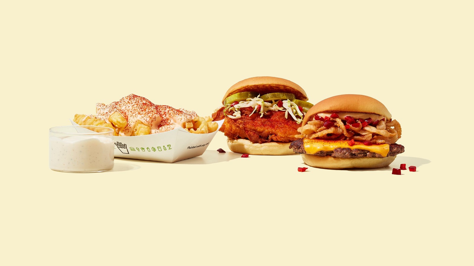 A tray of loaded fries next to two different Shake Shack burgers on yellow