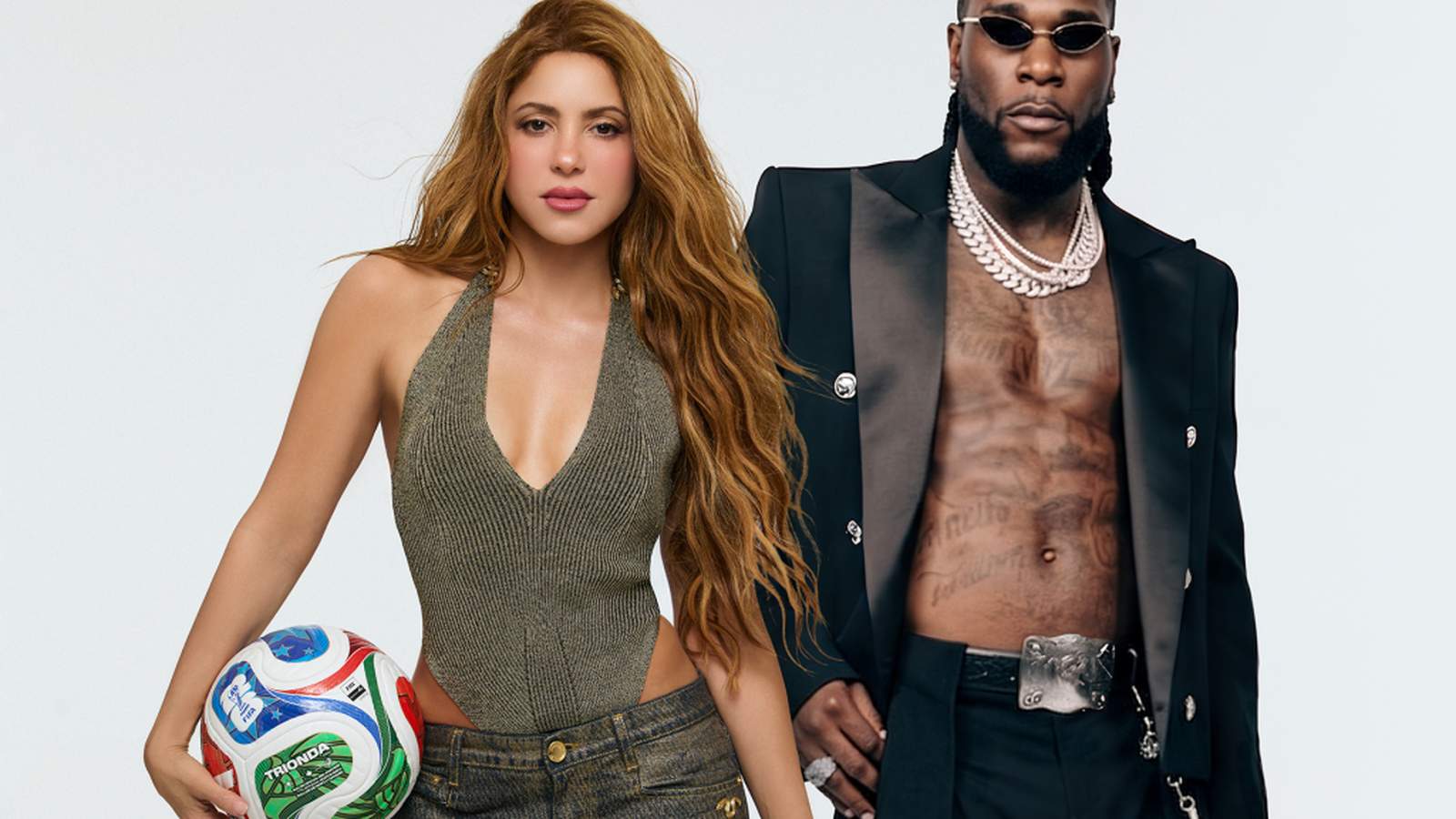 Shakira holding a soccer ball standing next to Burna Boy on white background