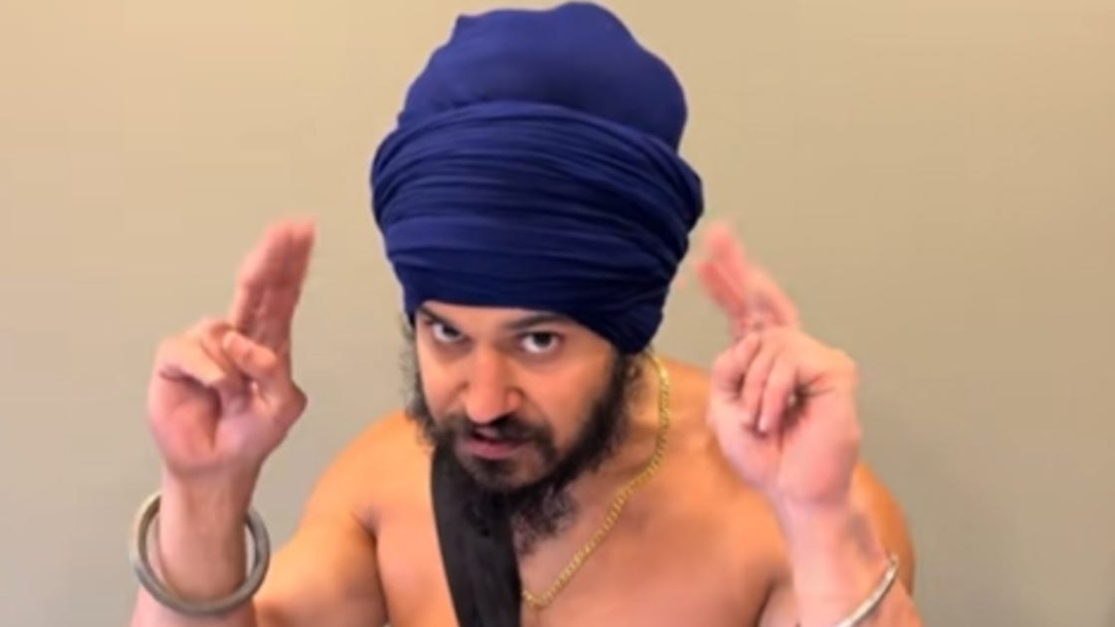 A Sikh man wearing a blue turban and kara gesturing with his hands